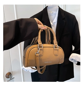 Détail d'un sac bowling en cuir marron à motif lychee tenu par un mannequin en costume