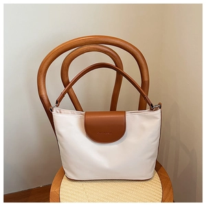 Detail of a minimalist tote bag featuring cream and caramel leather stitching on a wood chair