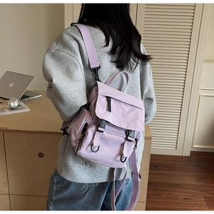 Back view of a lavender canvas backpack with multiple pockets on a female model