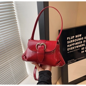 Close-up of a red patent leather saddle bag featuring a heart-shaped silver metal buckle