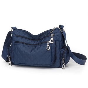 Detail of dark blue nylon crossbody bag featuring diamond quilting and silver metal zippers