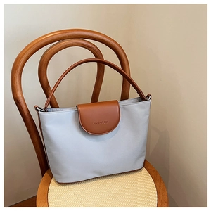 Detail of grey canvas tote with brown leather handles and brand logo on a wicker chair