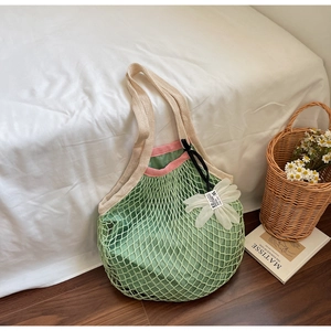 Detail of green mesh knit tote bag with flower charm and beige wide shoulder strap