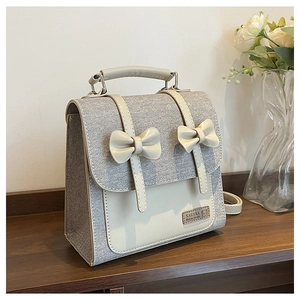 Detail of grey fabric backpack with cream faux leather flap and decorative bows on top