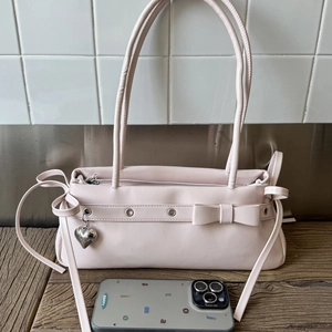 Detail of light pink faux leather shoulder bag with a bow and silver heart pendant