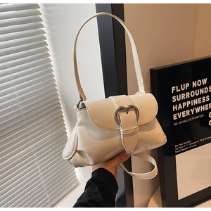 Detail view of cream-white saddle bag featuring a decorative silver heart-shaped buckle