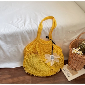 Detail of yellow mesh tote bag with 3D floral accent and black ribbon on white bedding