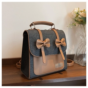 Detail of blue denim and brown leather backpack with bow accents on a wooden shelf