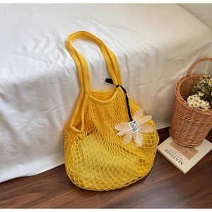 Detail of a yellow mesh knit tote bag with flower charm and ribbon on white bedding