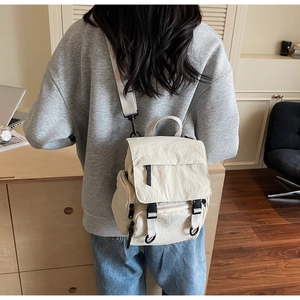 Versatile beige canvas backpack shown as a crossbody bag on model in a cozy studio setting