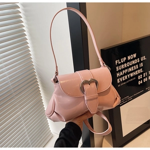 Close-up of pink saddle bag featuring a large silver heart-shaped metal buckle and soft pleats