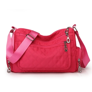 Close-up of rose red nylon crossbody bag with quilted diamond pattern and multi-zipper layers