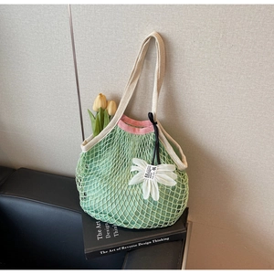 Detail of green mesh knit tote with pink trim and floral charm on art books