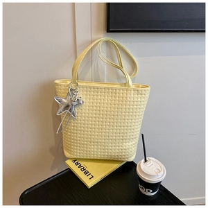 Detail of light yellow woven texture tote bag with a silver star charm and long strap