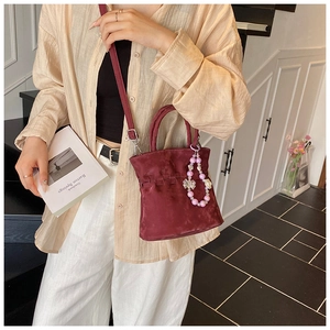Detail of burgundy pleated bucket bag with pearl charms and bow accessory on shoulder strap