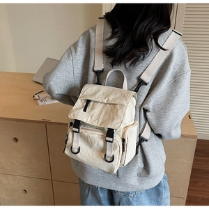 Close-up of cream nylon backpack featuring black plastic buckle straps and side zipper detail