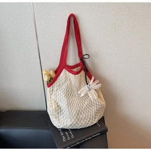 Detail of cream crochet beach bag with red strap and flower charm on art books