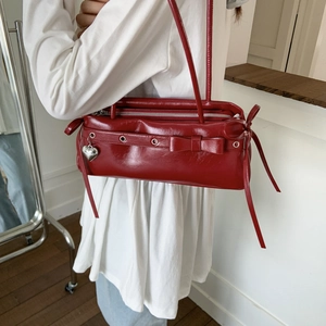 Close-up of red glossy leather shoulder bag with bow detail and silver heart charm