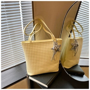 Detailed view of pale yellow woven tote bag with star pendant and tassel on books