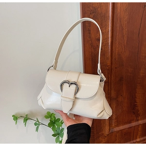 Detail of minimalist cream leather saddle bag with large silver heart-shaped metal buckle