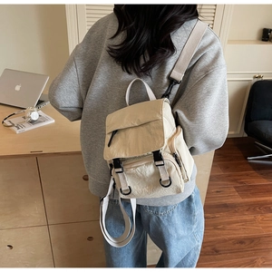 Detail view of the beige nylon mini backpack showing the zippers and side pocket texture