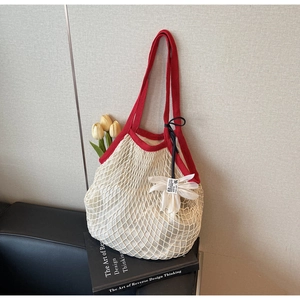 Detail of off-white mesh tote bag with red trim and floral pendant on a sofa