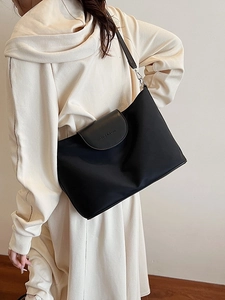 Minimalist black tote bag with leather flap and embossed logo shown on shoulder