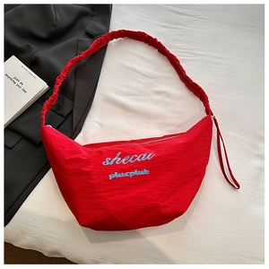 Detail of red crescent bag featuring blue embroidery and ruched elastic shoulder strap