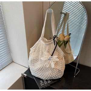Detail of a beige knit mesh tote bag featuring a white floral charm and inner fabric liner