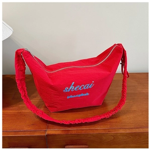 Detail view of a red pleated nylon crescent bag with a gathered shoulder strap on wood
