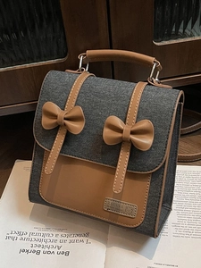 Retro grey denim backpack with caramel leather straps and bow details on vintage wood