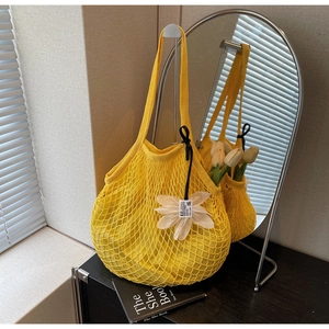 Close-up of bright yellow crochet mesh tote with a delicate white floral charm