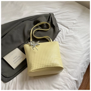Detail of light yellow woven bucket bag with silver star charm on white linen