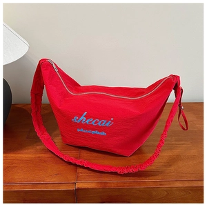 Detail of red pleated shoulder bag with blue shecai lettering on wooden table