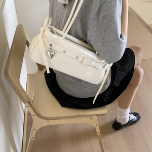 Detail of cream shoulder bag featuring side bow ties and silver heart pendant