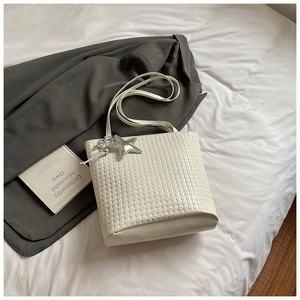 Close-up of white woven bucket bag featuring silver star charm on a bed sheet
