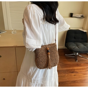 Dettaglio della borsa a tracolla in paglia marrone con nappe boho e perline in legno