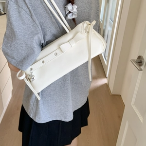 Detail of white leather baguette bag with bow decoration and silver heart pendant