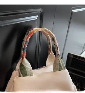 Détail des poignées en sangle jacquard colorée sur un sac à bandoulière en nylon beige
