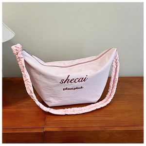 Detailed close-up of light pink crescent bag with scrunchie strap on wood surface