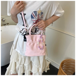 Detail view of pink bucket bag with woven edges and decorative beaded charm