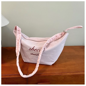 Detail of light pink pleated shoulder bag with red shecc text on a wooden surface