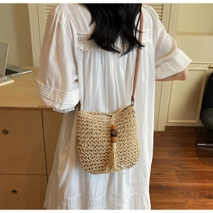 Dettaglio borsa a secchiello in paglia intrecciata con nappa boho e perline di legno