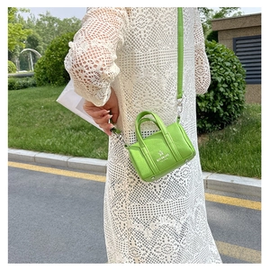 Close-up of bright green litchi grain mini pillow bag worn with a white lace dress