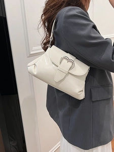 Minimalist cream saddle shoulder bag with silver heart buckle worn with a gray blazer