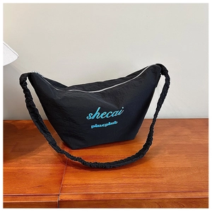 Detail of black pleated half-moon bag with blue embroidery and shirred strap on wood