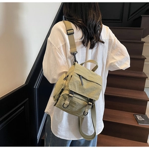 Rear view of a model wearing a green multi-pocket canvas crossbody backpack on stairs