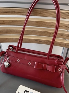 Burgundy faux leather shoulder bag with a bow detail and heart pendant on gray background