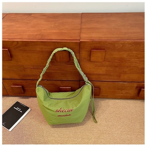 Detailed view of green pleated hobo bag with red embroidered lettering on wood background