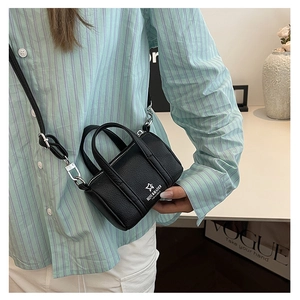 Detailed view of mini black lychee leather pillow bag worn as a crossbody with silver hardware